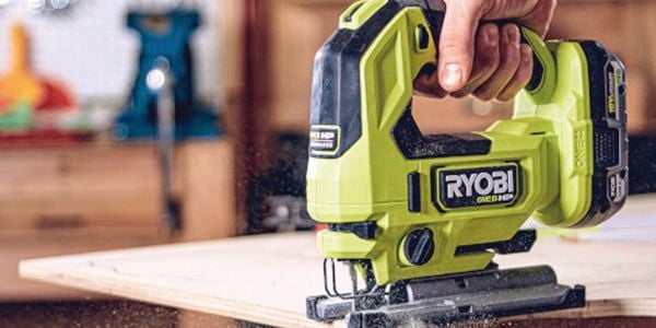 A person cutting a wooden board using a jigsaw.