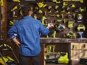 A man looking at a pegboard with lots of green Ryobi tools mounted on the wall of his garage