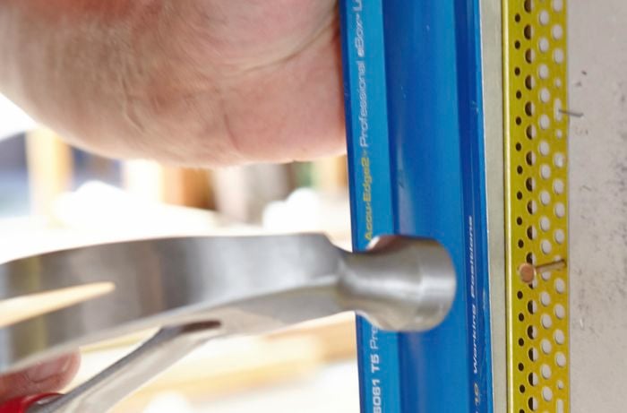 Person hammering nail through hole in metal external angle piece.