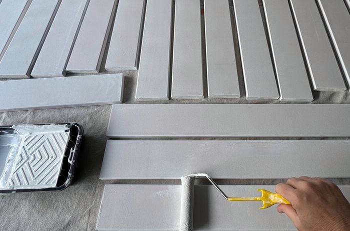A hand using a roller to paint decking boards white