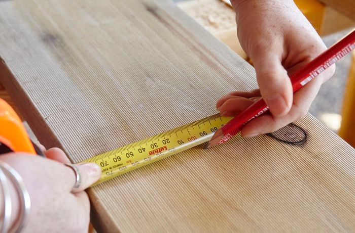 A person marking a length of timber using a measuring tape and pencil