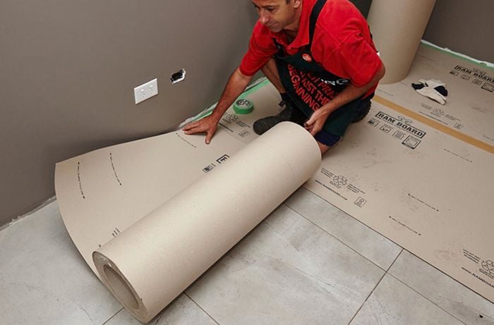 A person unrolling a roll of floor protector on a tiled floor