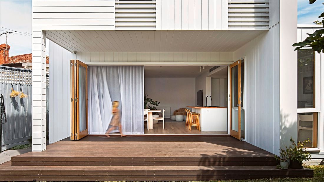 Two storey home with white panelled cladding, and a deck and lawn in the backyard.