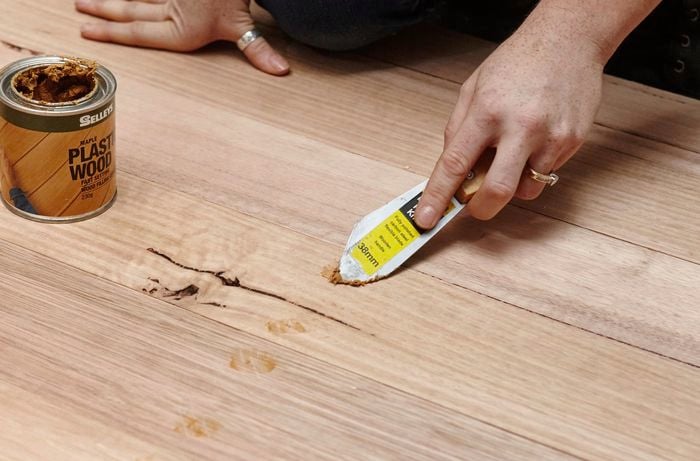 Person using wood filler to fill up holes in timber bedhead.