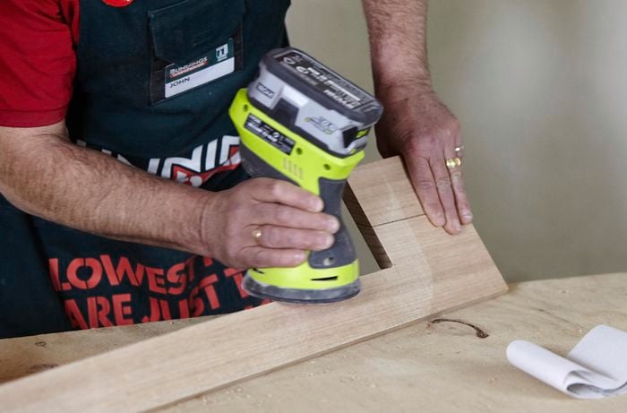 A cordless sander being used to work a piece of timber