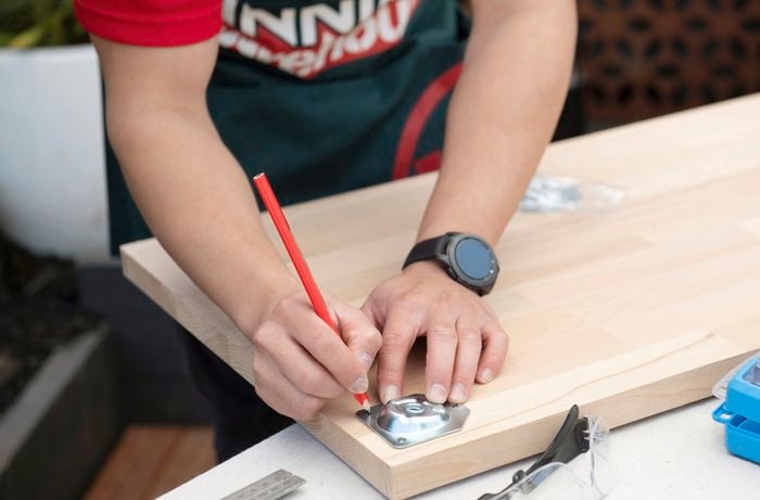 Points on the underside of a desk being marked for drilling, with a leg plate being used as a guide