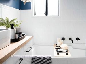 A white tiled bathroom, with black tapware over a white bath and a deep blue feature wall showcasing a bathroom design idea.
