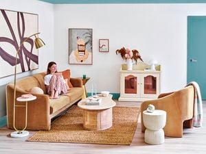 Person sits on a brown sofa couch in a white walled room with blue ceiling and trim.