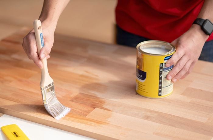 A person in a red T shirt is using a brush to apply timber oil to the benchtop. ]