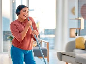 Woman wearing headphones, holding a broom in a lounge room.