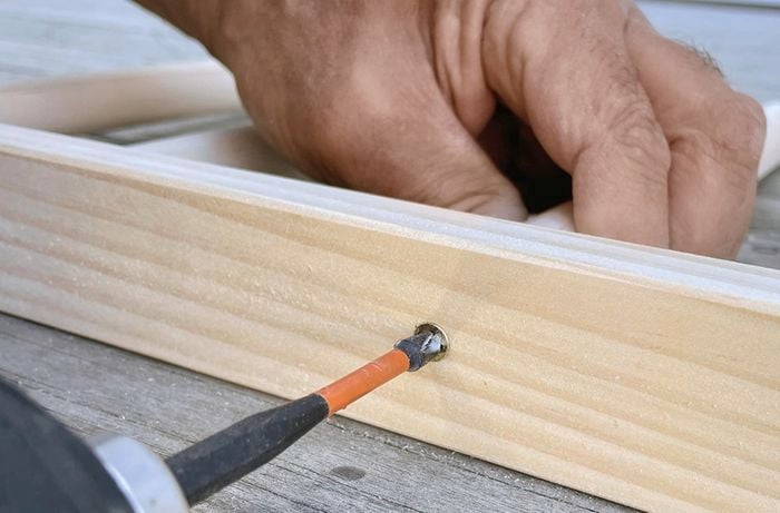 Close up of a pair of hands securing dowel into pine with a screw