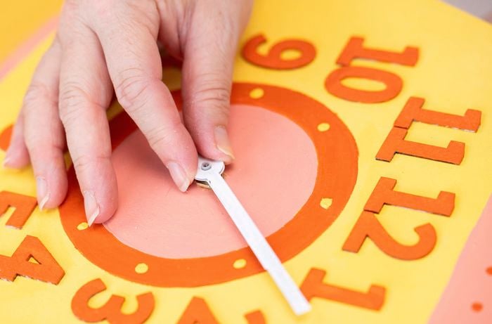 A person is inserting the clock body into the circular opening so it fits neatly within the frame.