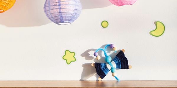 A D.I.Y. Bluey craft Flappy project sits on a timber shelf with a star, moon, planet and two Bluey lanterns about it.