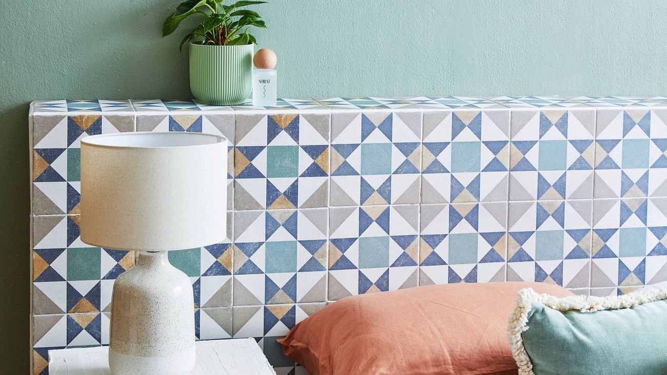 A close up of a light coloured tiled D.I.Y. bedhead with a green plant on top, and white side table and lap