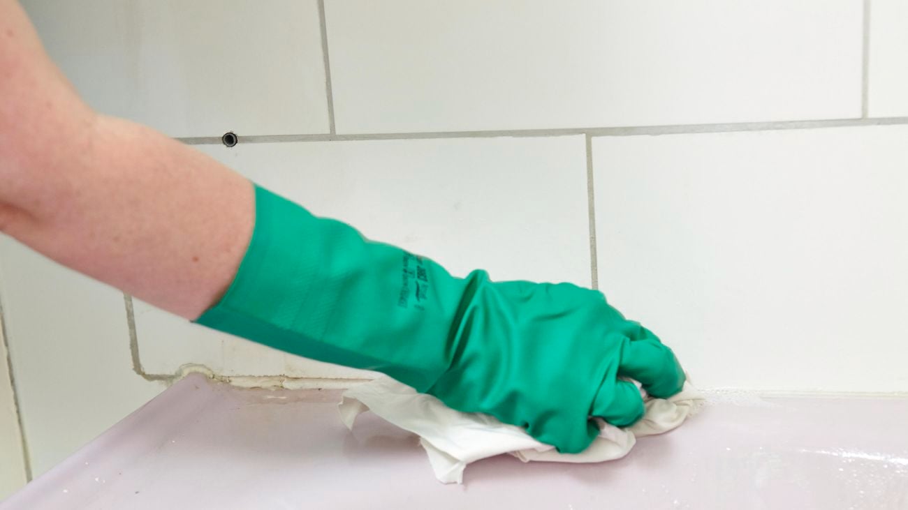 Person wiping grout around a bath with a cloth