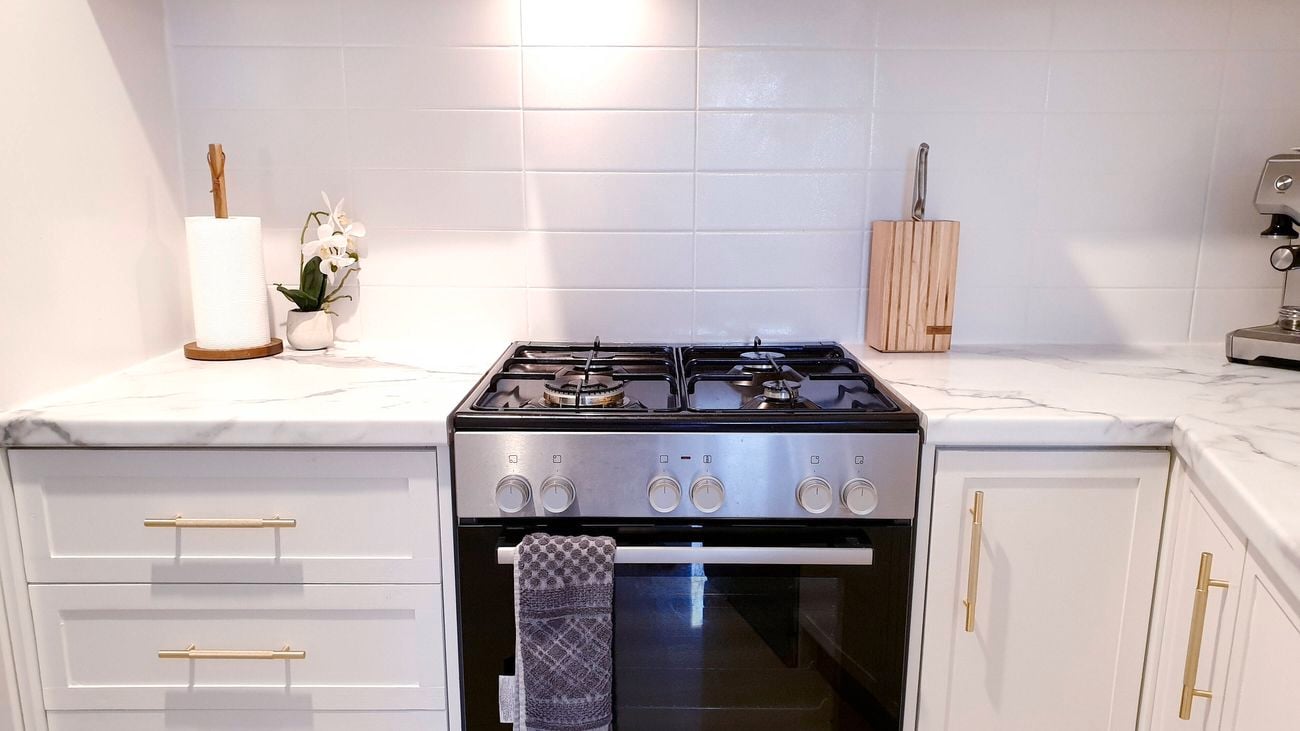 An after image of the renovated kitchen with white cupboards and a white marble benchtop.