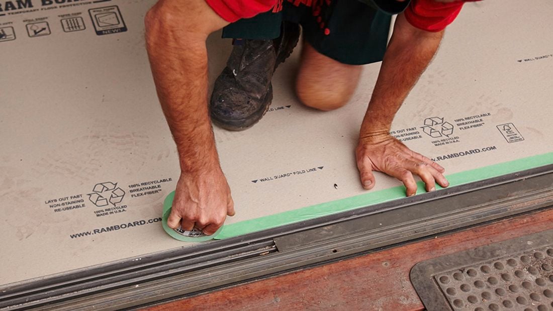 A person taping floor protector along a doorway opening