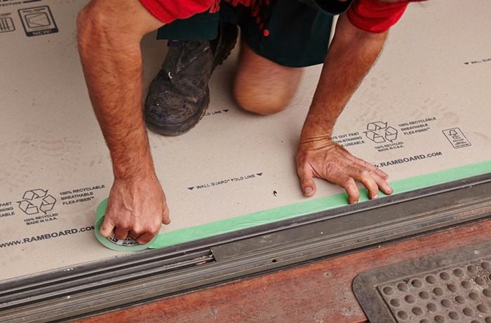 A person taping floor protector along a doorway opening