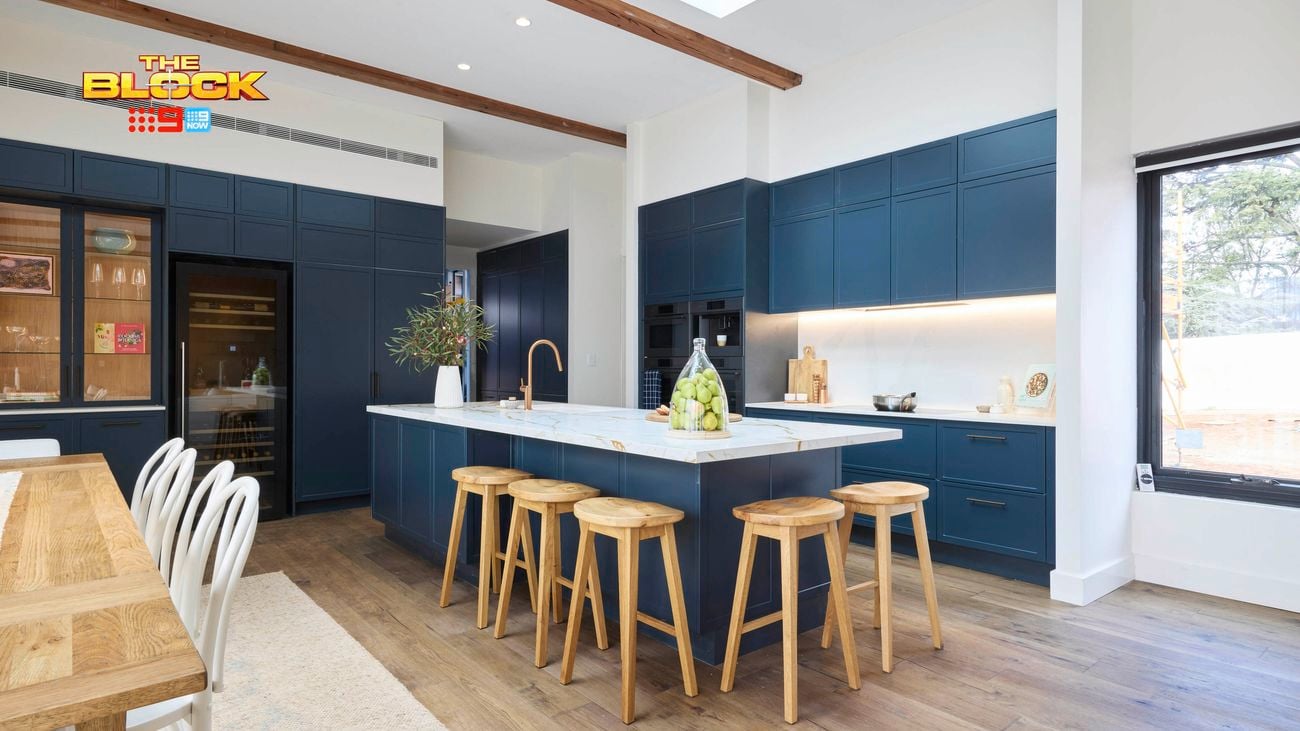 Modern kitchen with navy cabinetry, white island, and wooden stools.