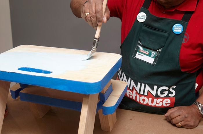 Person using paint brush to paint DIY wooden step stool light blue.