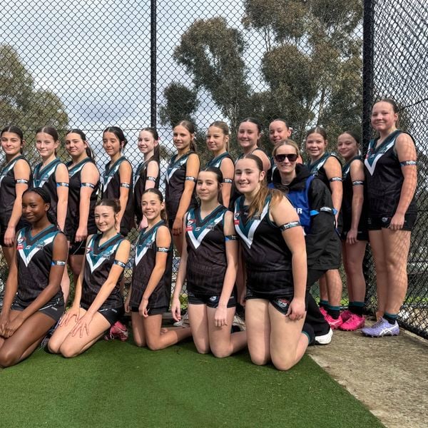 Group of netball players in black and blue uniforms posing together beside an outdoor court.