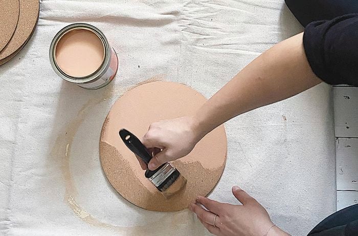 A pair of hands painting a cork mat on a drop sheet