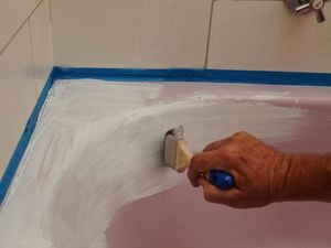 A person painting a pink bath with white paint using paint brush