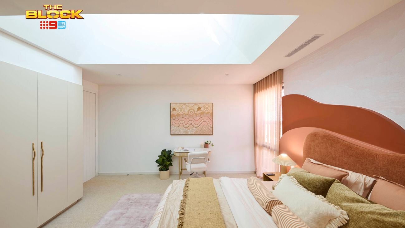 Cream bedroom with a queen bed, desk and wardrobe on a blush rug and a red and orange hill style bedhead.