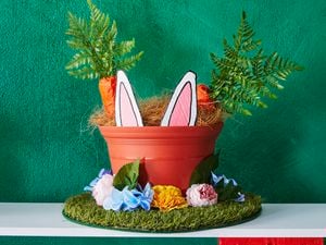 A Bunnings straw hat decorated with artificial turf, a plastic pot and faux carrots, flowers and bunny ears for Easter.