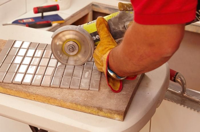 An angle grinder being used to cut holes in a sheet of mosaic tiles for tap fittings or power outlets