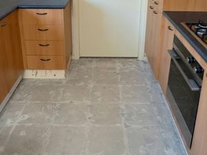 A kitchen floor exposes a clean concrete surface after the tile removal surrounded by wooden cabinets.