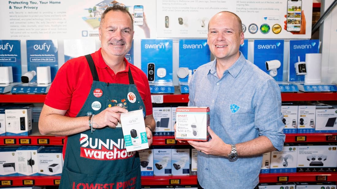 Bunnings team member wearing an apron in store standing next to a representative holding home security products.