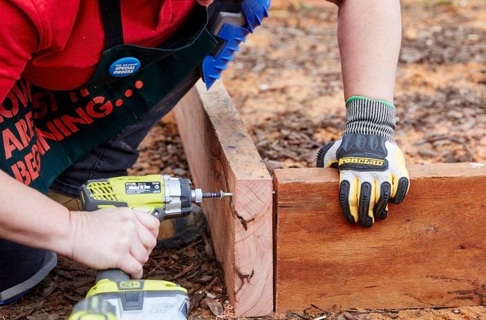 A timber sleeper being drilled into the frame for a sleeper compost bin with a power drill