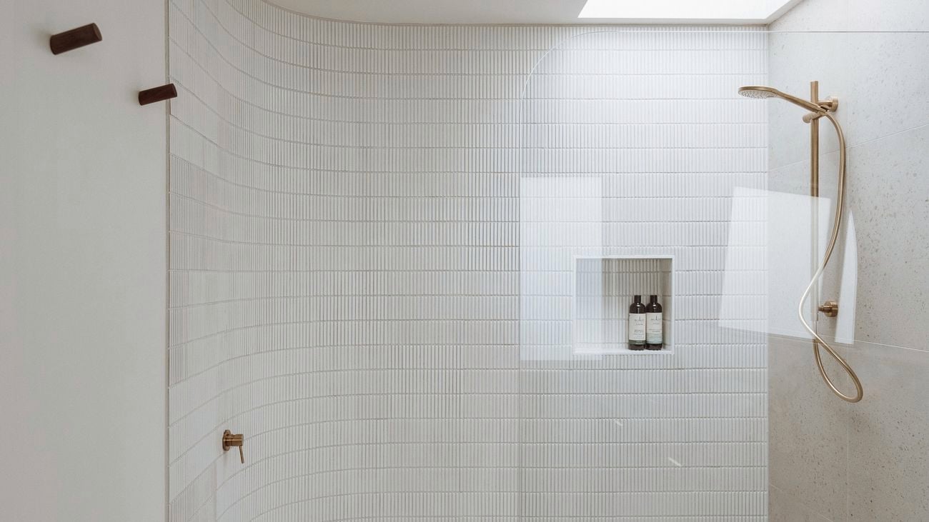 Modern white curved shower with a gold showerhead and glass door.