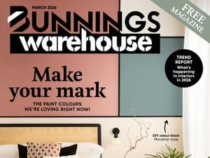 A magazine cover titled ‘Bunnings Warehouse’ with the headline ‘Make your mark.’ The cover features a styled bedroom with a rattan-style bedhead, layered bedding, patterned cushions, a side table with decorative items, indoor plants, and colour-blocked wall panels. A small dog sits on the rug at the foot of the bed. Additional headings promote paint colours, DIY ideas, and renovation inspiration.