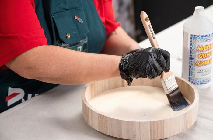 A Bunnings Team Member holding a paint brush against a top of a side table