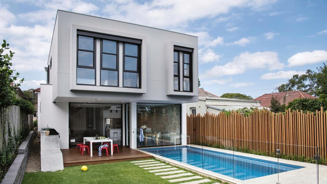 A backyard with a lawn, pavers, pool and deck.