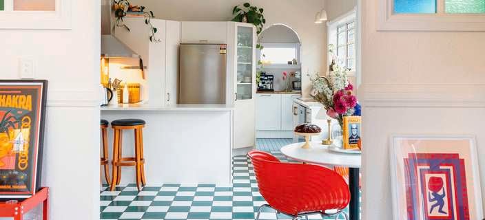 A vibrant kitchen with a green-and-white checkered floor, white cabinetry, a red dining chair and colourful stained-glass windows.