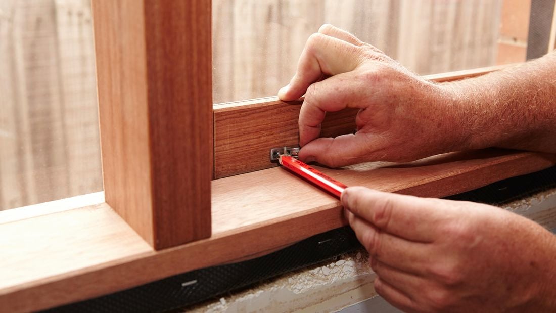 A person marking the position of a window stay on a timber window using a pencil