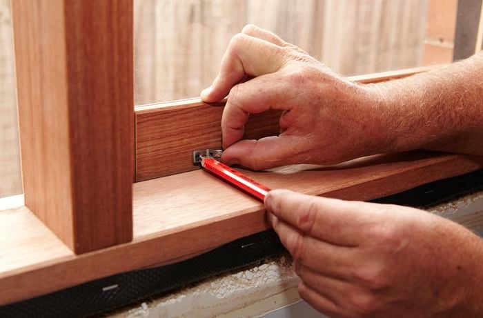 A person marking the position of a window stay on a timber window using a pencil