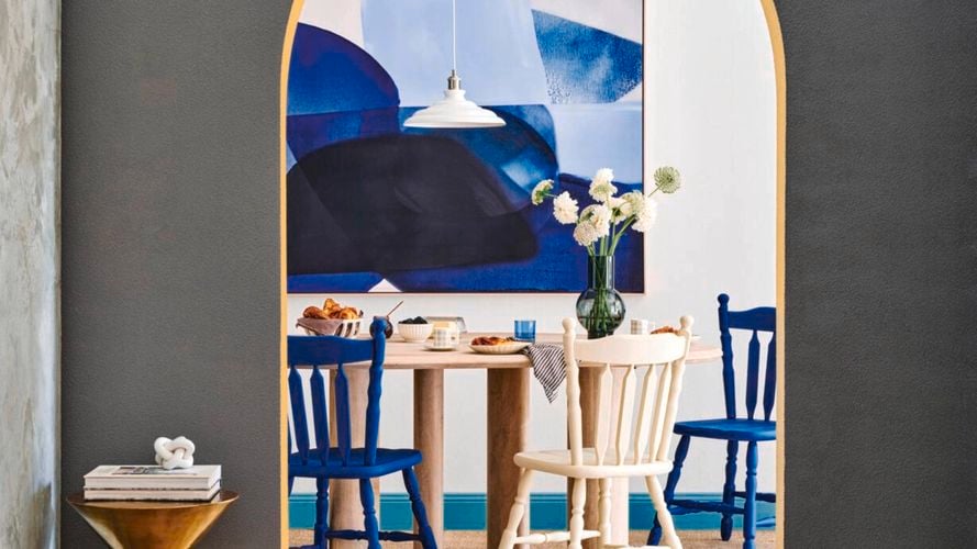 Dining room with timber round table, colourful timber chairs, flower in a vase sitting in the dining table