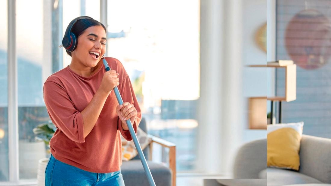 Woman wearing headphones, holding a broom in a lounge room.