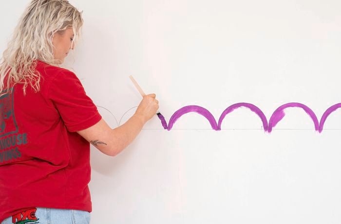 A Bunnings team member is carefully painting curved scallop shapes along a marked guideline.