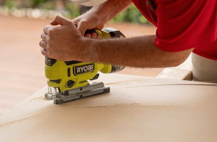 A person is cutting an arch shape out of an MDF sheet with a jigsaw.