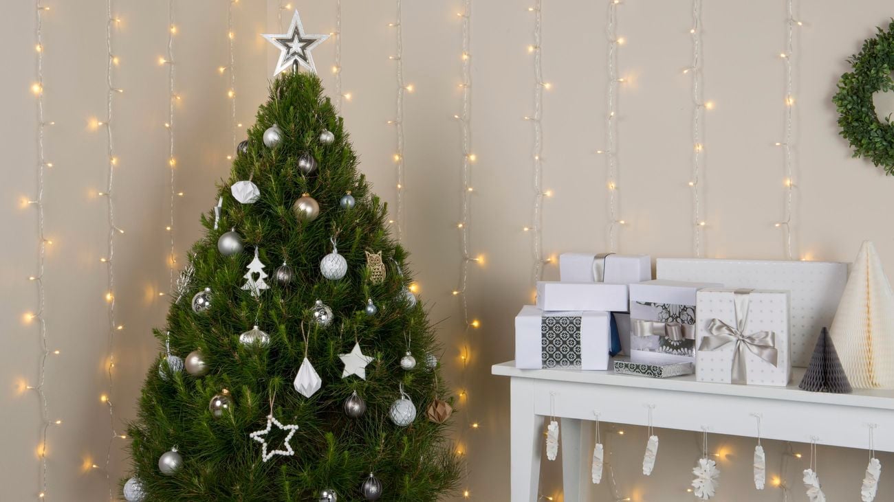 Decorated Christmas tree next to a table of presents and cascading fairy lights on the wall