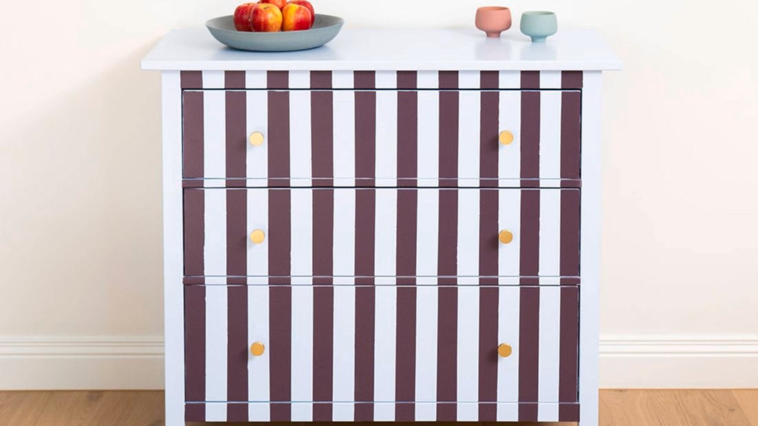 Small cabinet with vertical burgundy and white stripes, photographed front-on against a plain wall.