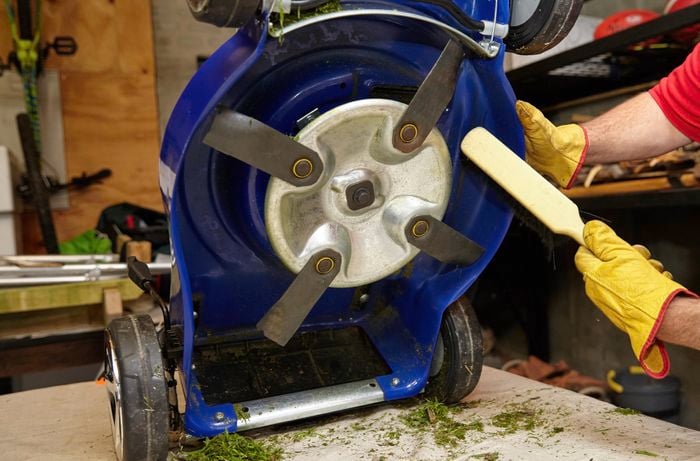 A person cleaning the underneath of a lawn mower with a brush