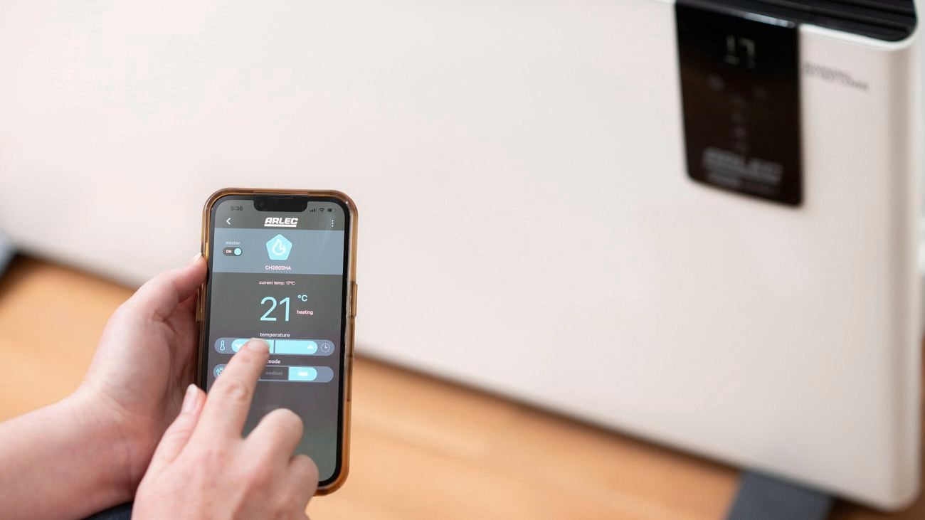 A hand is remotely controlling a heater from a phone.