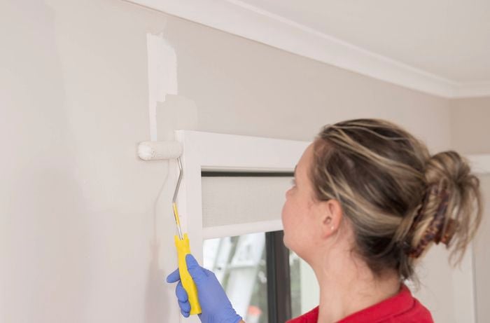 A person wearing gloves is using a small paint roller to apply primer and paint over the repaired area