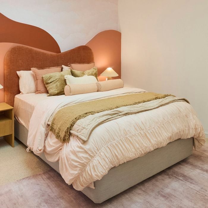 Cream bedroom with a queen bed, desk and mirror on a blush rug and a red and orange hill style bedhead.
